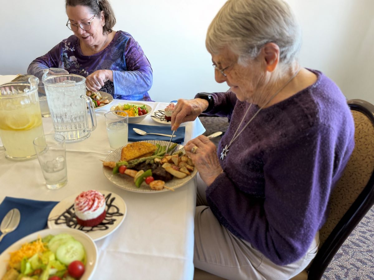 Senior females are seated at a lunch table with plates of food.