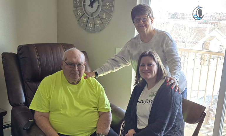 nurse with senior patient on a chair and a family member in the background