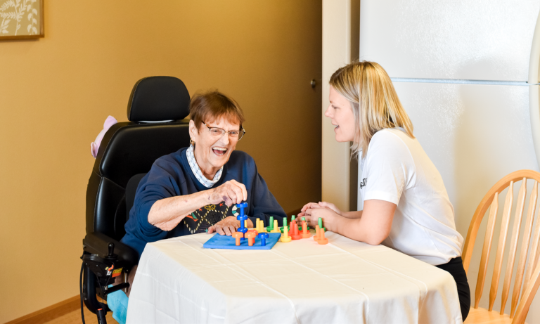 Senior woman laughing with caregiver in a warm home setting, showing trust, comfort, and compassionate senior care.