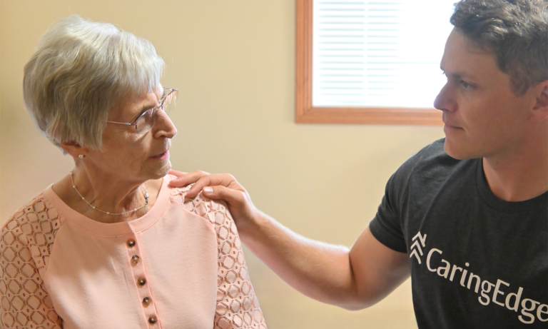 A hospice team member rests a hand on an older woman’s shoulder as they talk.